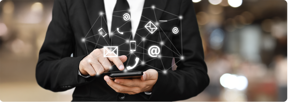 A team at a modern office desk surrounded by multiple devices showing emails, chats, and notifications, representing scattered communication channels.